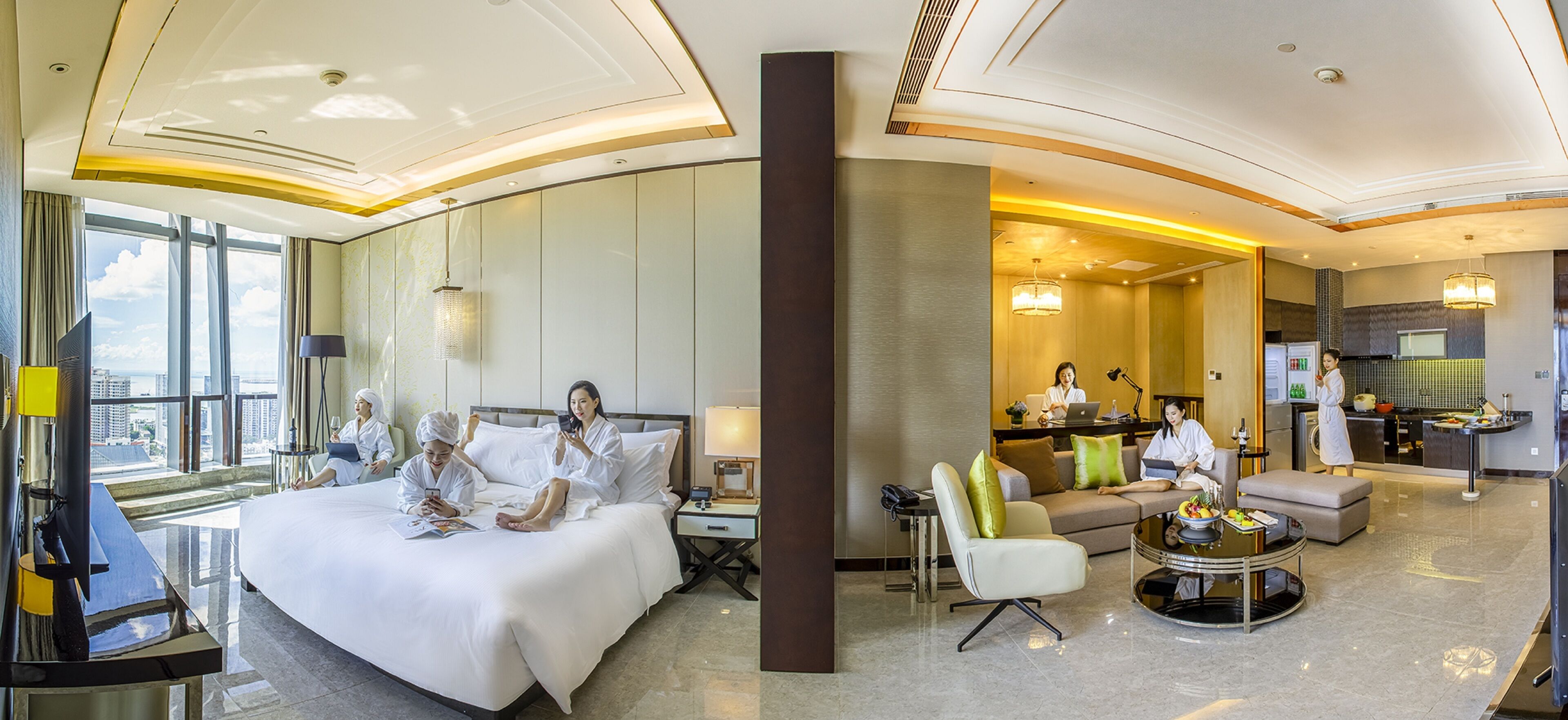 A hotel room with a large bed, a sitting area with a sofa and coffee table, a kitchenette, and a view of the city.