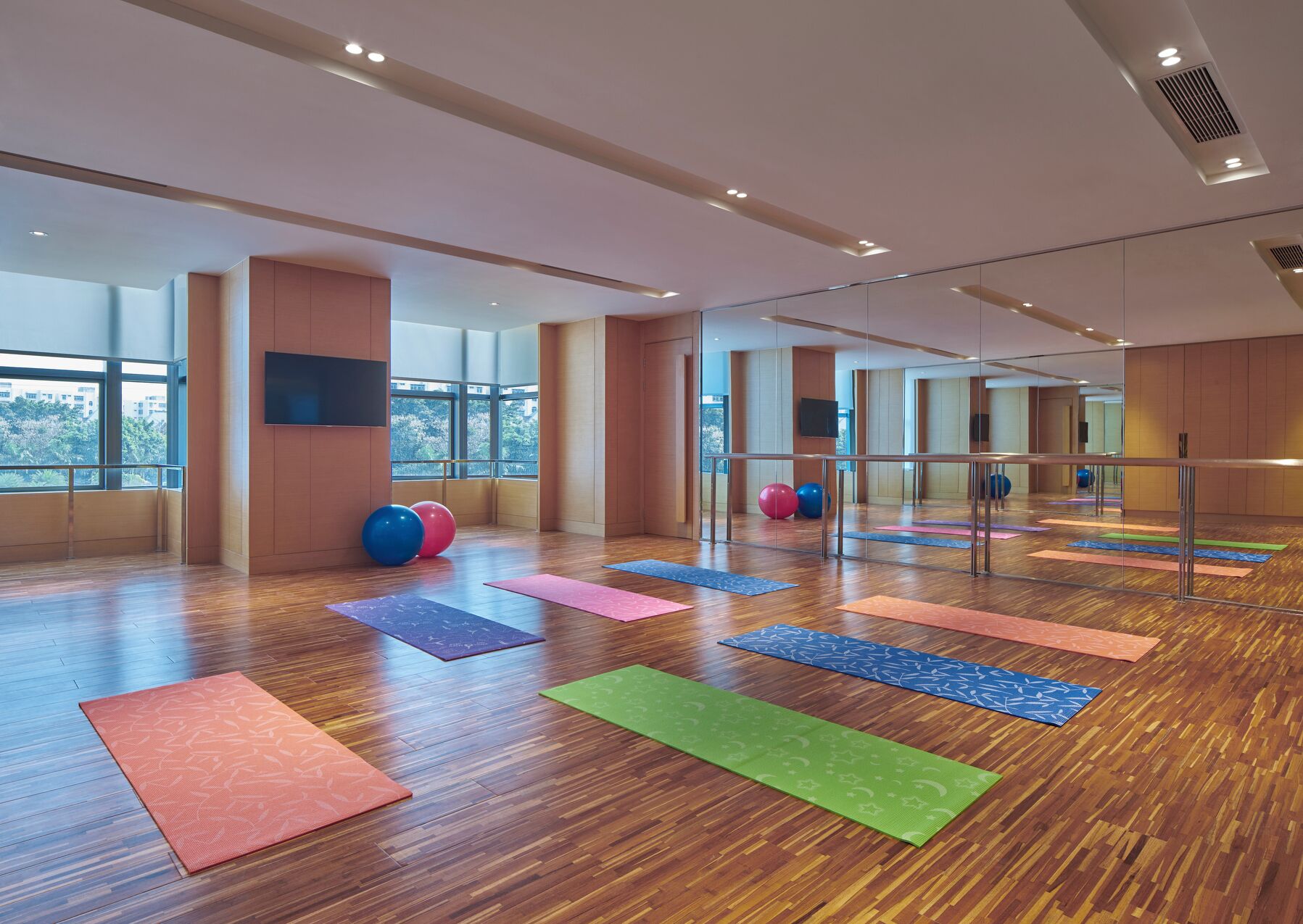A spacious indoor gym with exercise mats, large windows, and a mirrored wall.