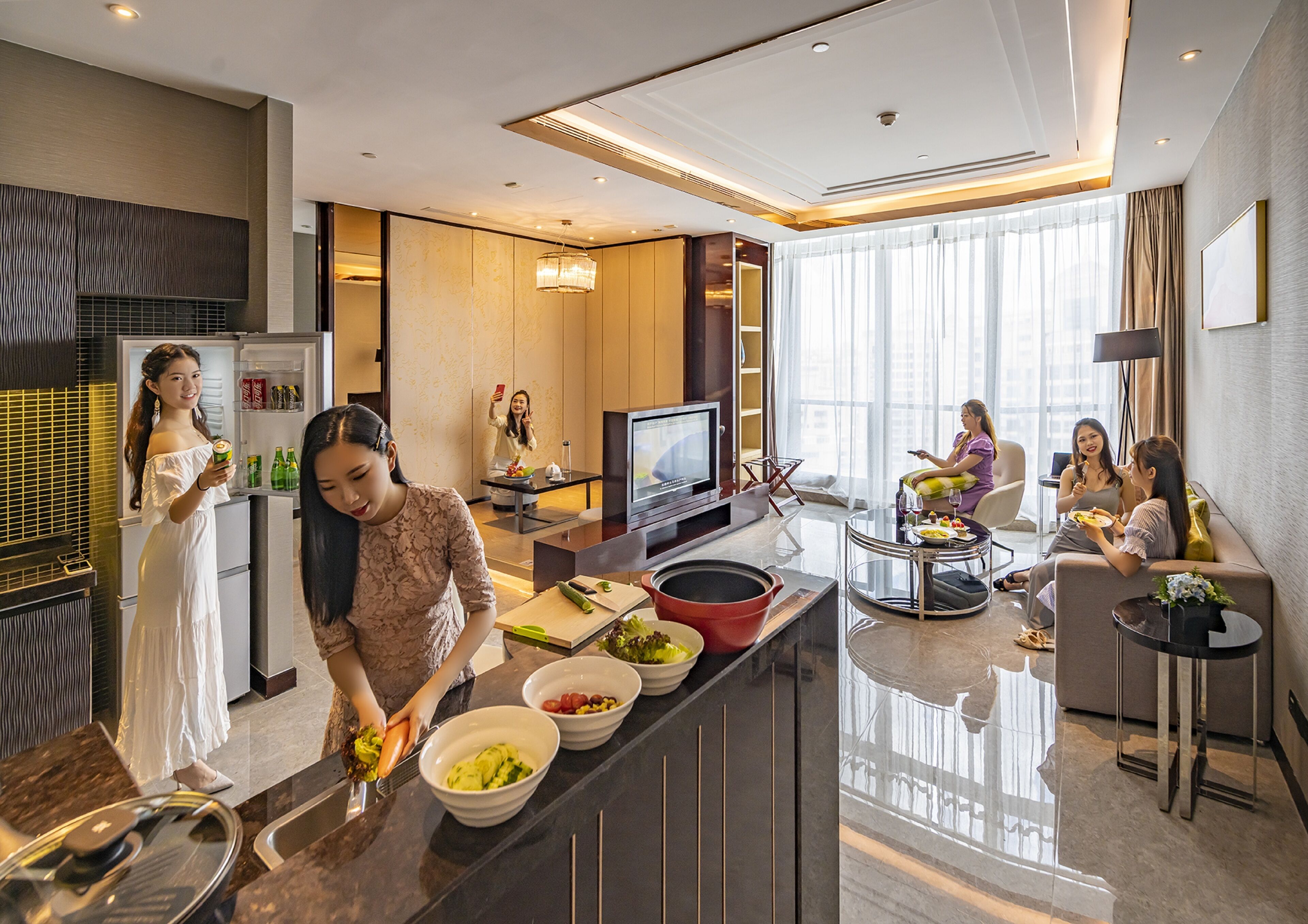 Une cuisine moderne équipée d’un réfrigérateur, un coin repas avec un téléviseur et un espace d étente avec un canapé et une table.