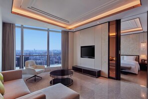 A modern hotel room with a large window, a flat-screen TV, a sofa, a coffee table, and a bed.