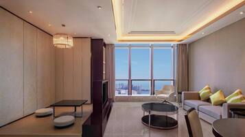 A modern living room with a sofa, ottomans, a coffee table, a TV, and a large window with a city view.