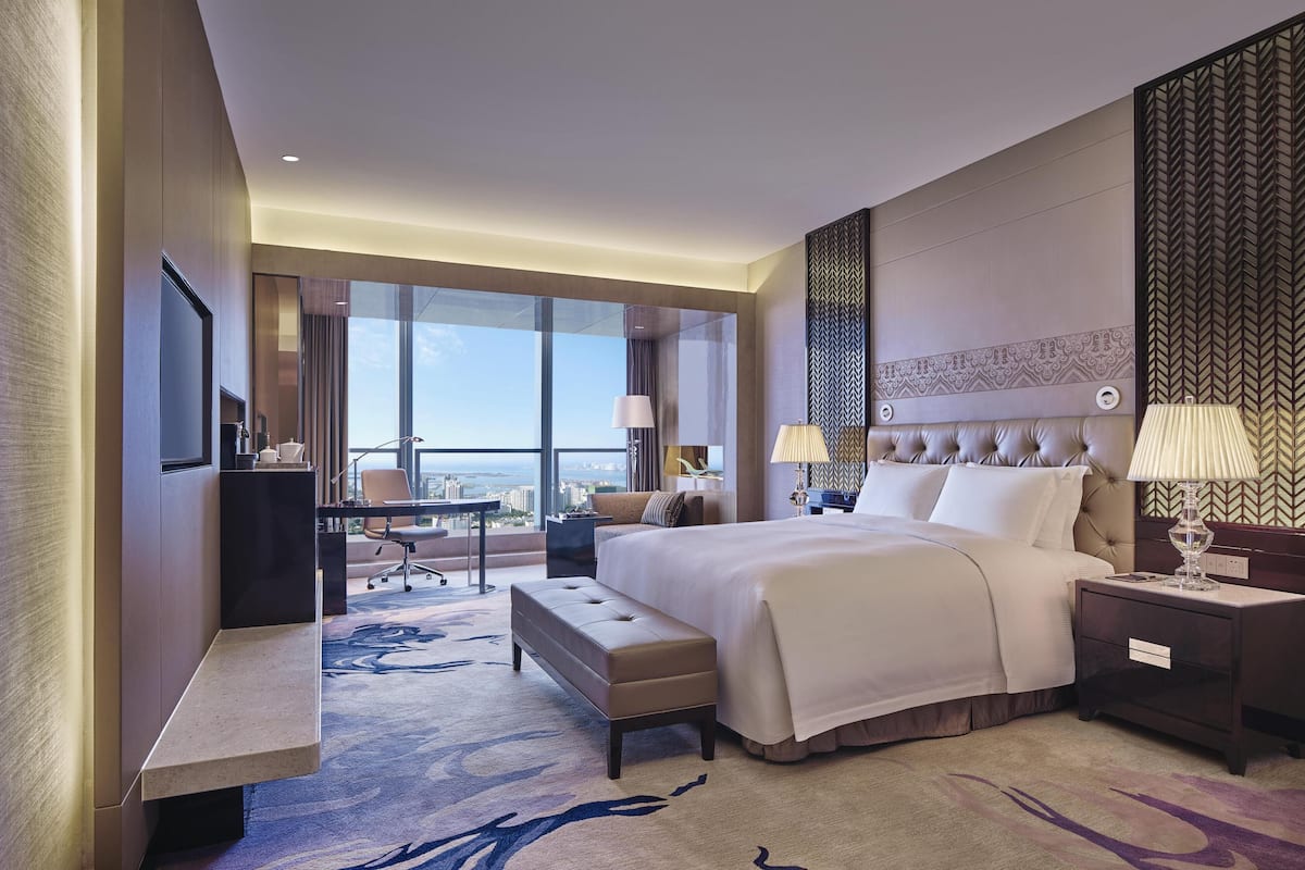 Una habitación de hotel moderna con una cama grande, un escritorio, una silla, un televisor y vistas a la ciudad.