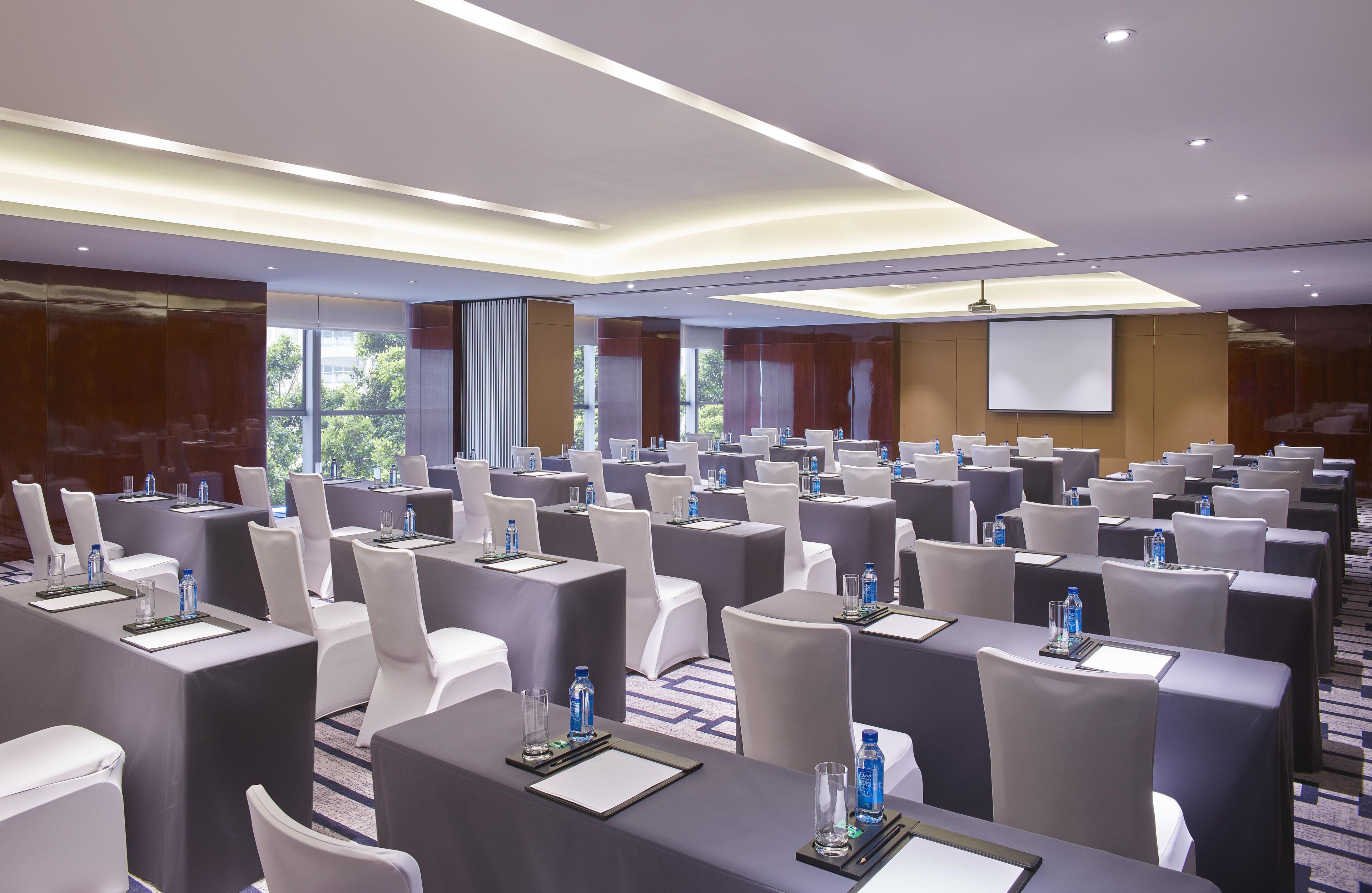 Un salón de conferencias con varias mesas, sillas y una pantalla para proyector.