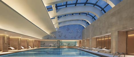 Piscina interior con techos altos y tragaluces, rodeada de zonas de descanso con asientos.
