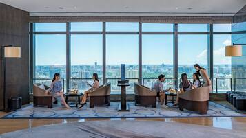 A modern hotel room with large windows, a city view, and a central table with a tiered dessert stand.
