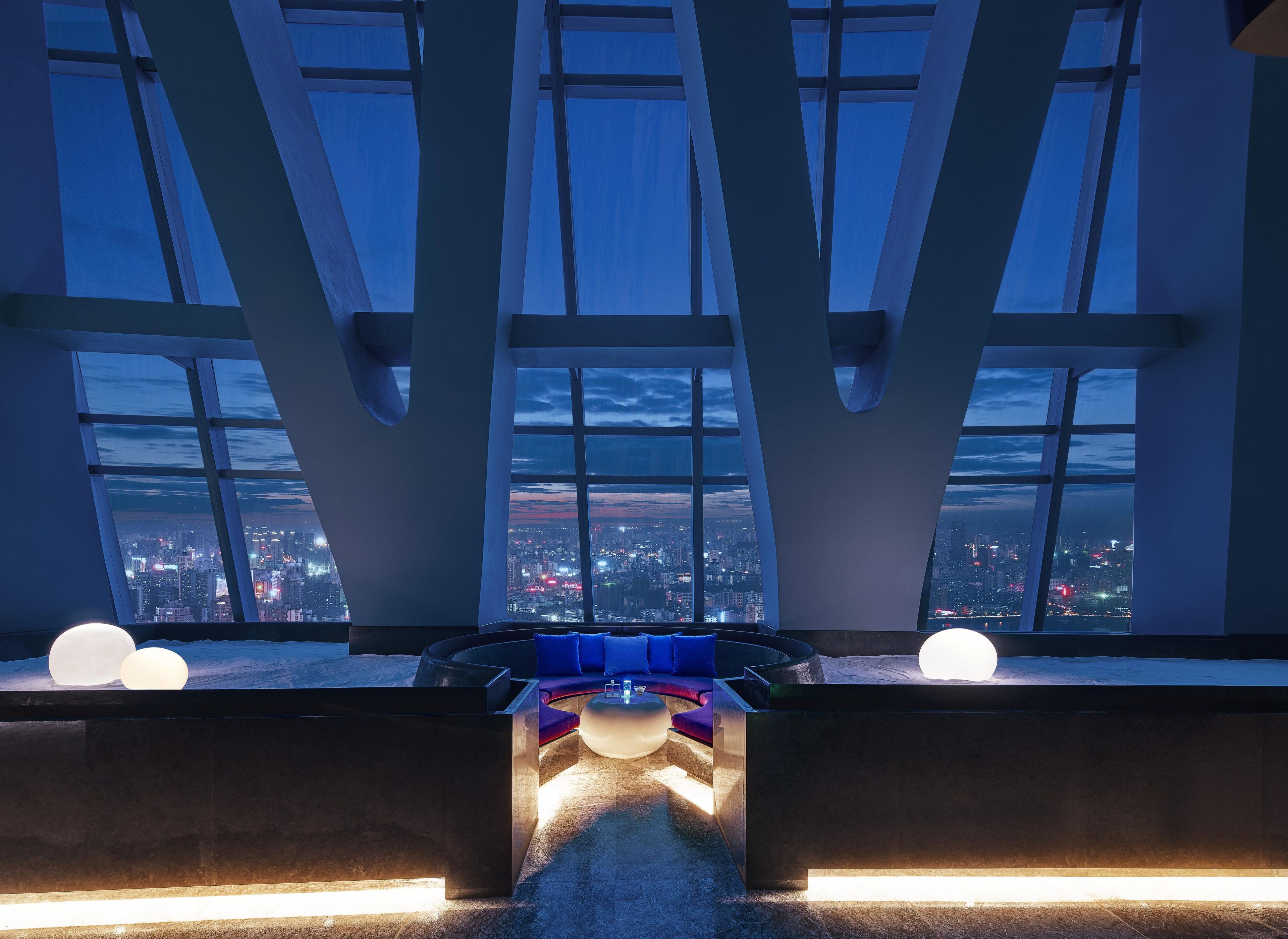 A modern interior with a panoramic city view through large windows, a central seating area with a sofa and a coffee table, and a minimalist design.