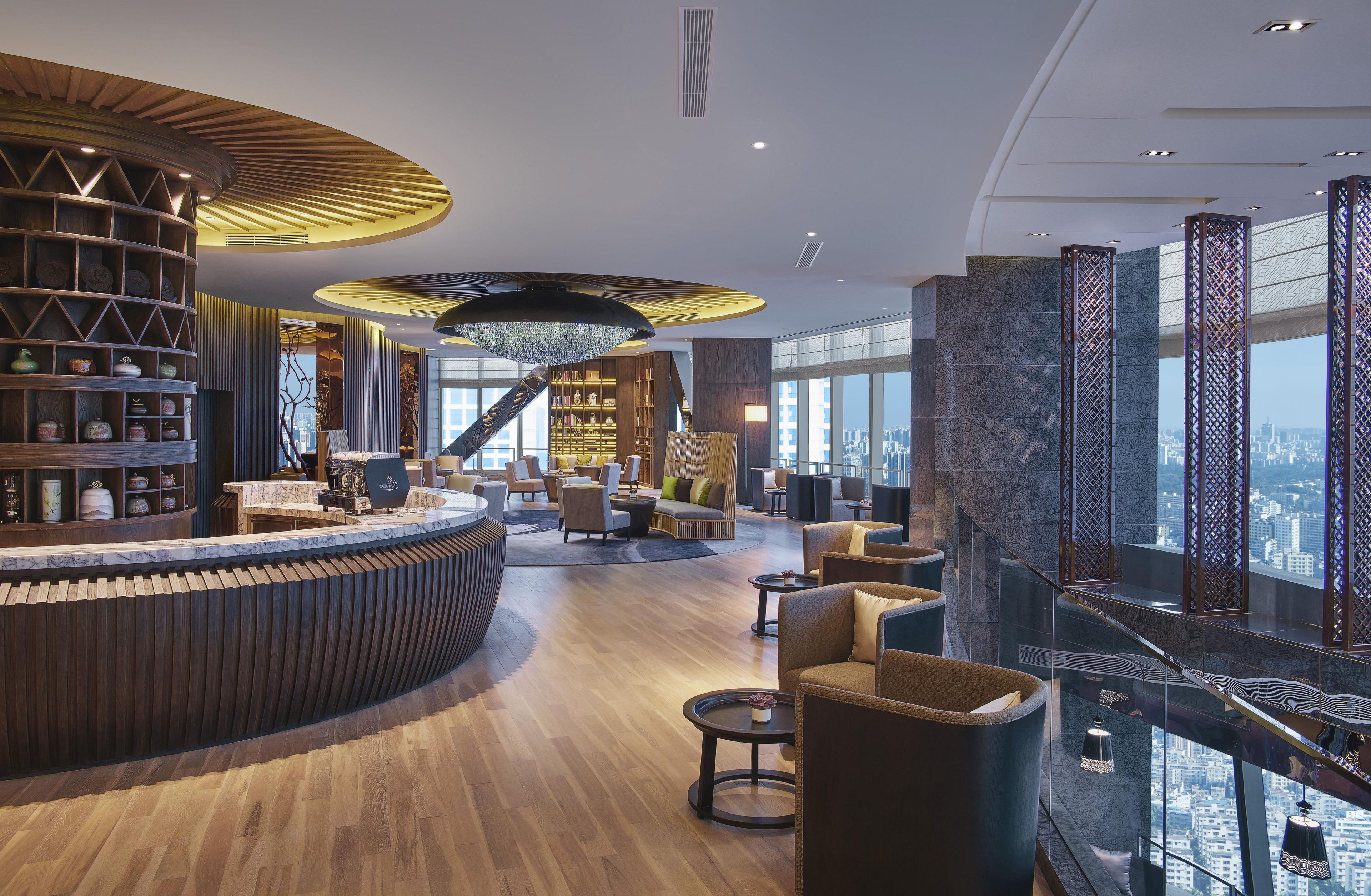A modern hotel lobby with a curved reception desk, a staircase, and a city view.