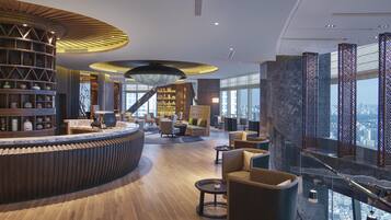 A modern hotel lobby with a curved reception desk, a staircase, and a city view.