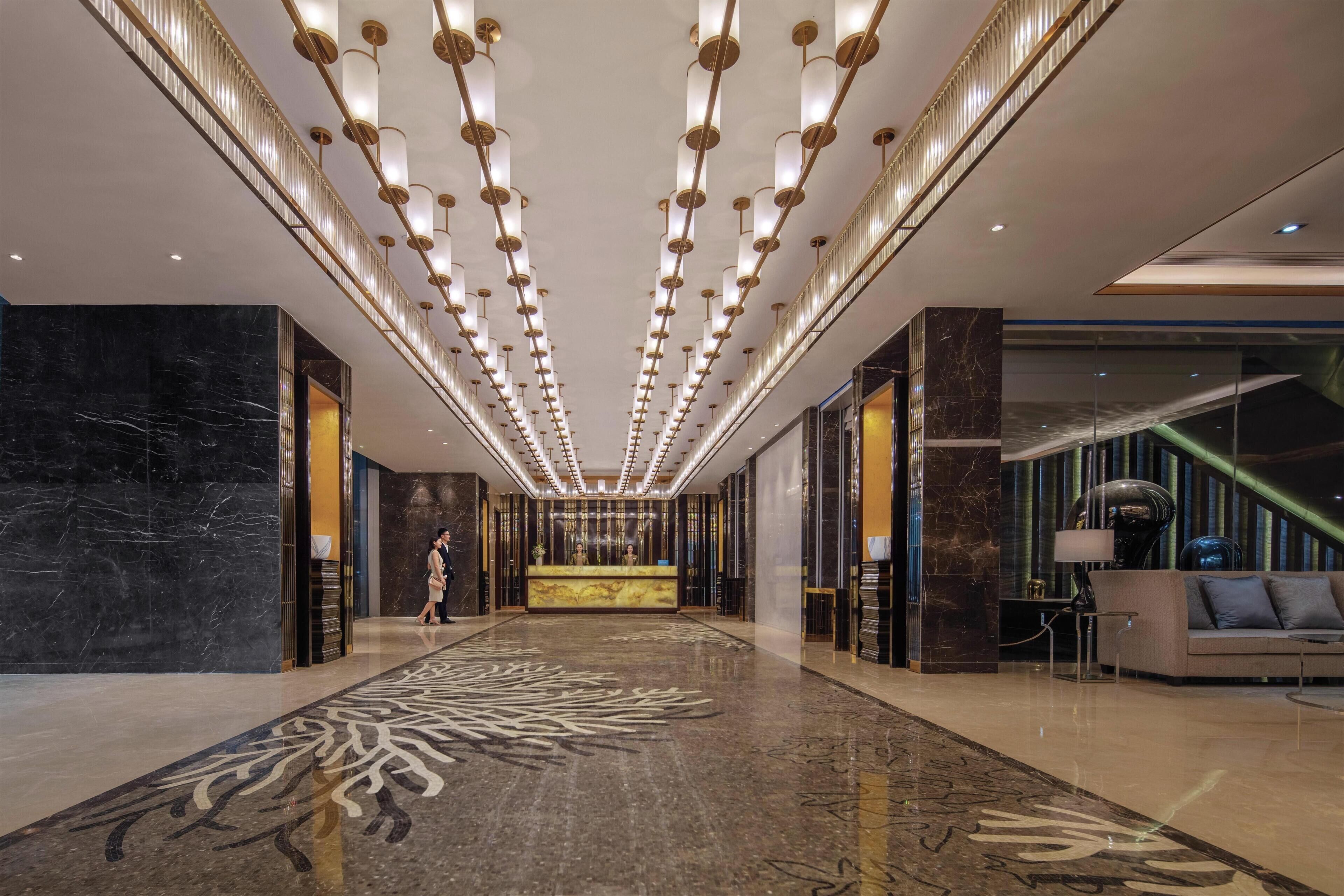 A spacious lobby with a marble floor, a reception desk, and a staircase.
