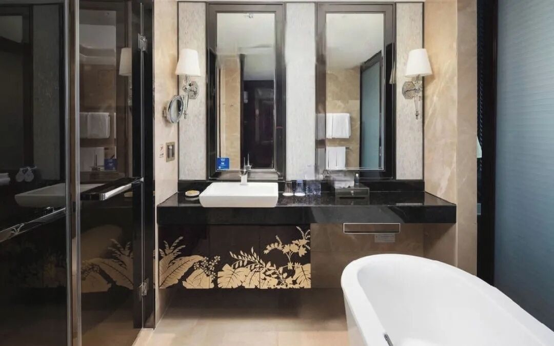 A modern bathroom with a large mirror, a white bathtub, and a black countertop with a sink.