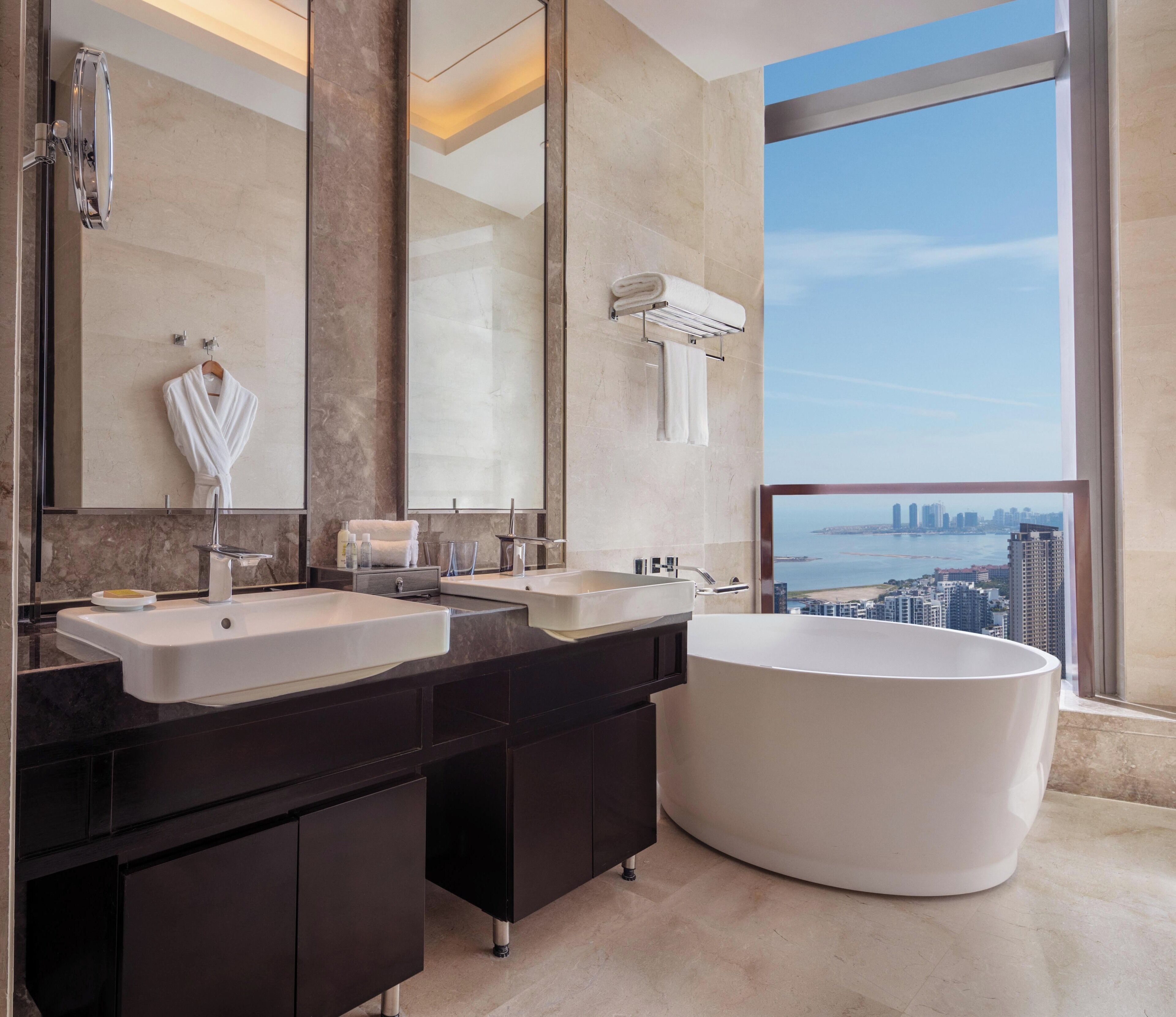 Un baño moderno con dos lavamanos, una bañera grande y vistas a la ciudad.