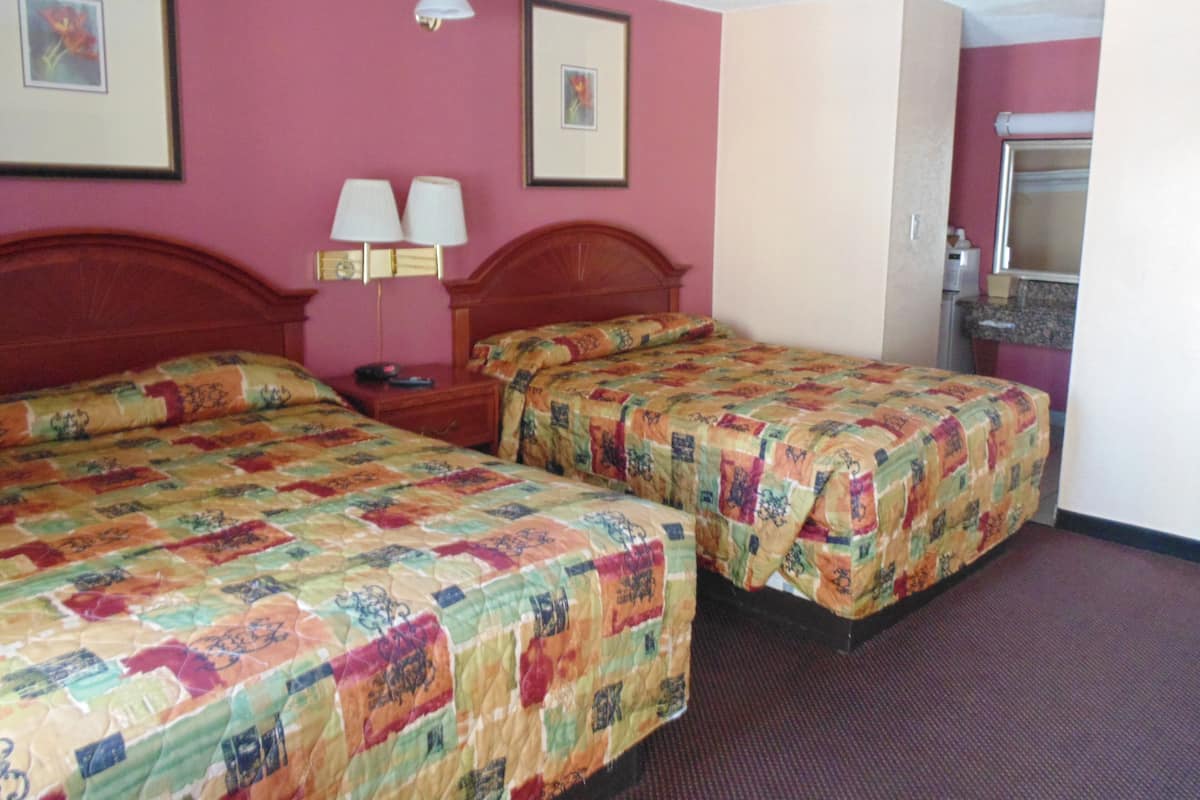 Quarto de hotel com duas camas, uma mesa de cabeceira, uma luminária e um banheiro visível por uma porta aberta.