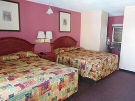 Habitación de hotel con dos camas, una mesita de noche, una lámpara y un baño a la vista a través de una puerta abierta.