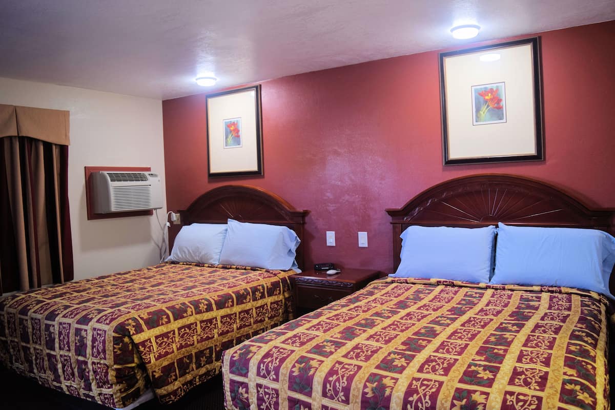 Duas camas de casal com roupa de cama estampada, ar condicionado fixado na parede e quadros decorativos.