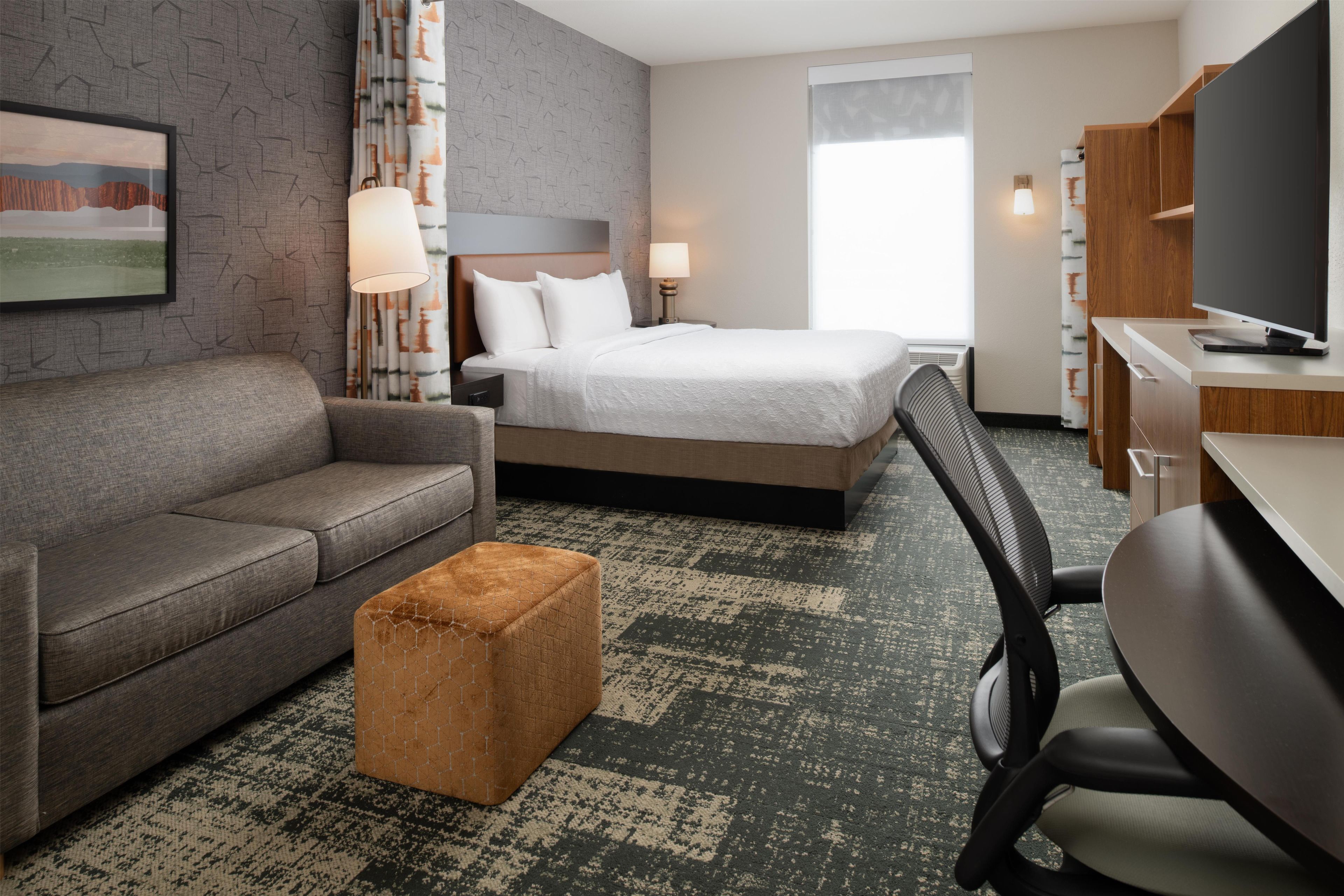 Ein Hotelzimmer mit Bett, Sofa, Schreibtisch, Stuhl, Lampe und Fernseher.