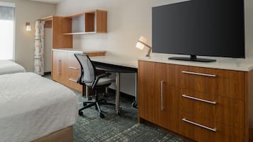 Quarto de hotel com cama, escrivaninha, cadeira, televisão e armários de madeira.