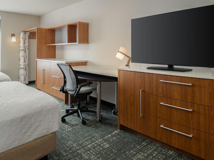 Habitación de hotel con cama, escritorio, silla, televisor y armarios de madera.