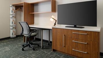 Habitación de hotel con escritorio, silla, televisor y armario.