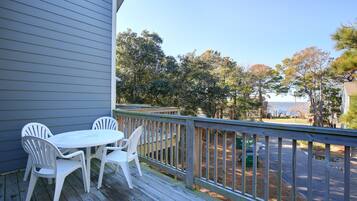A wooden deck with a table and chairs, overlooking a street and trees.