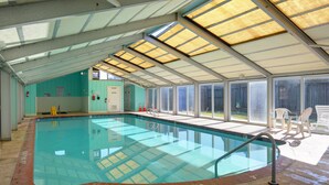 An indoor swimming pool with clear glass walls, a tiled floor, and a roof with skylights. - Ocean Pines Resort (Kitty Hawk)