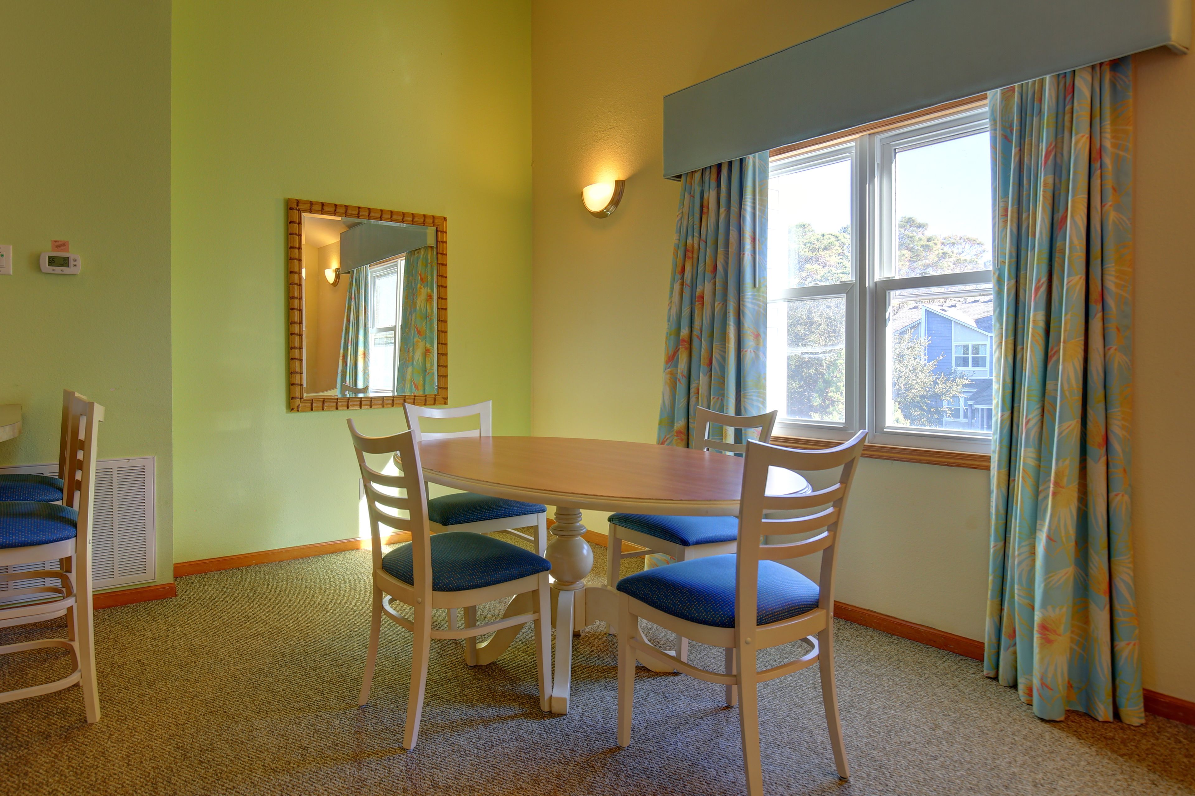 A dining room with a wooden table and chairs, a mirror, and a window with curtains.