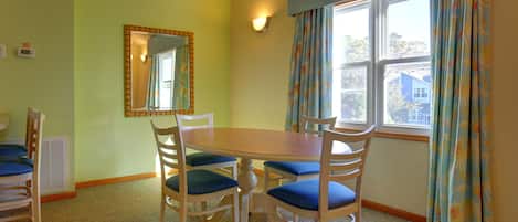 A dining room with a wooden table and chairs, a mirror, and a window with curtains.