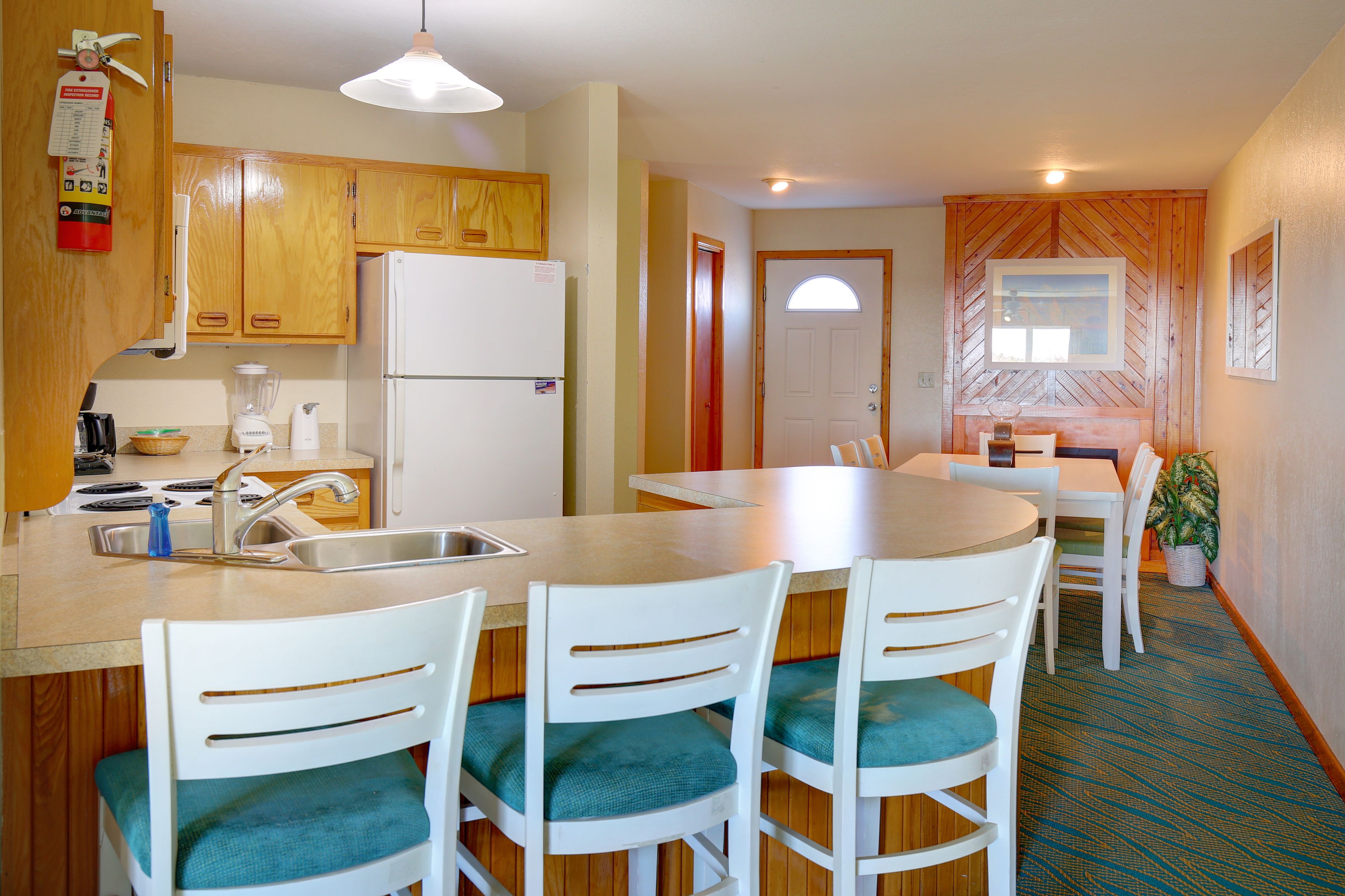A compact kitchen with wooden cabinets, a refrigerator, a sink, and a dining area with white chairs and a table.