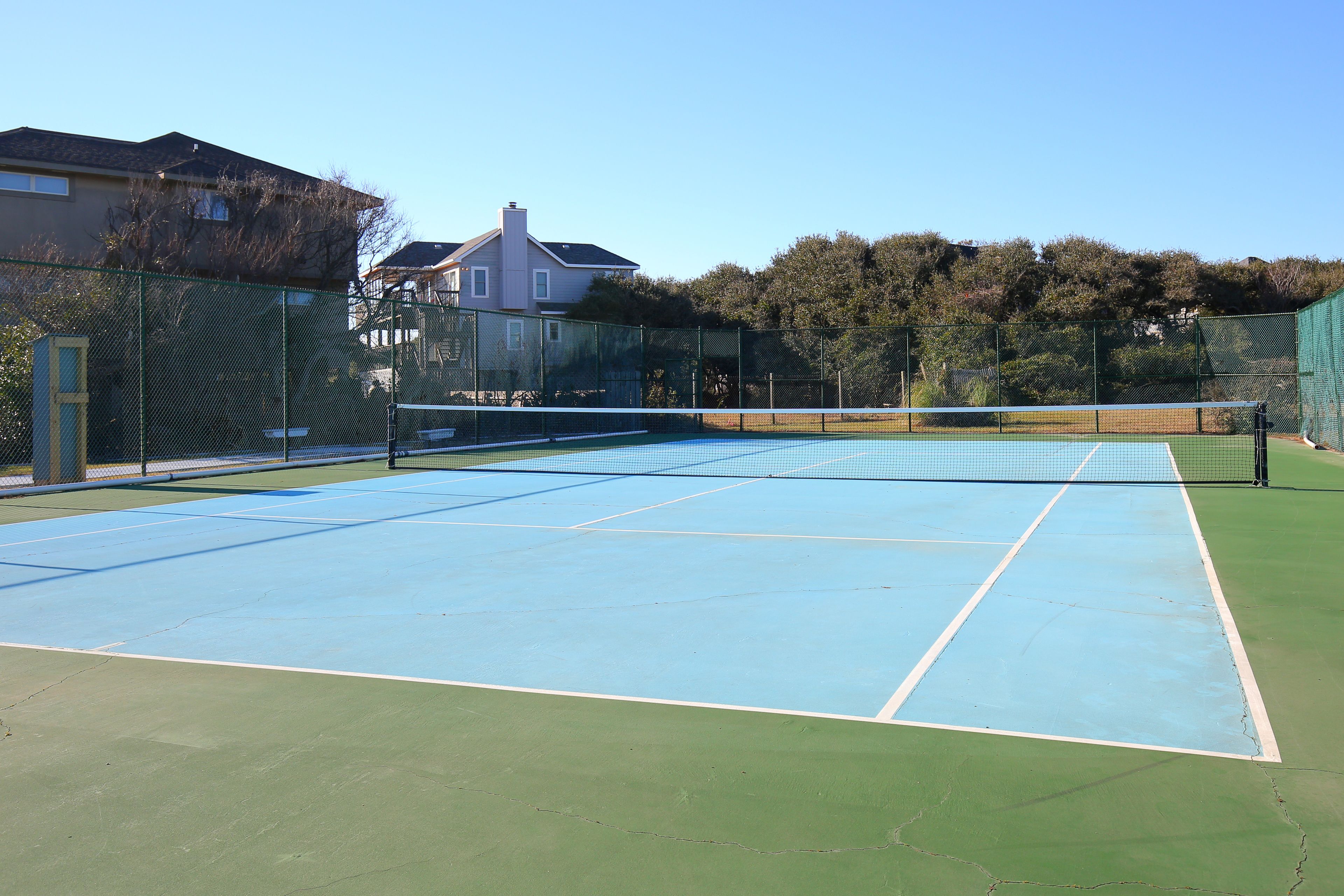 Ein Tennisplatz mit Netz, umgeben von einem grünen Zaun und Bäumen.
