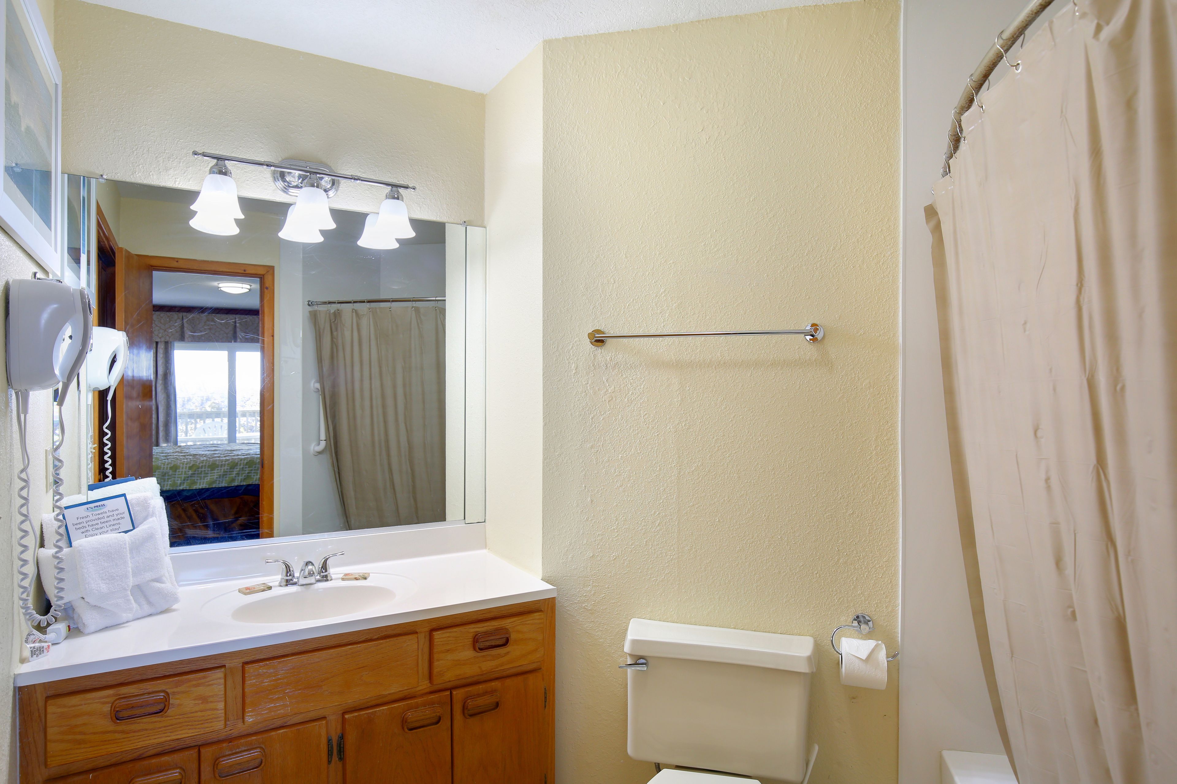 A bathroom with a sink, mirror, and toilet. There is a towel rack above the toilet and a shower curtain.