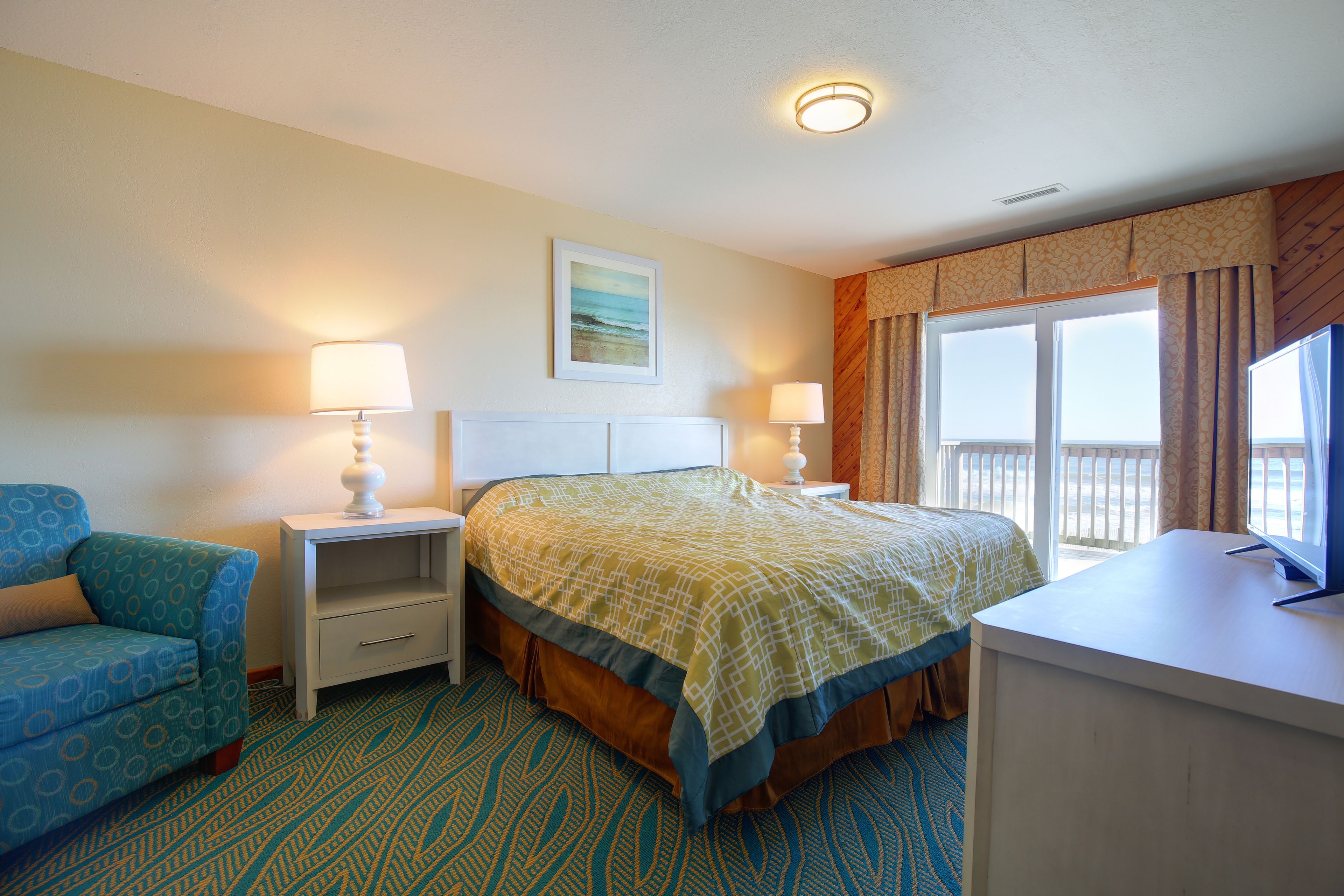 A hotel room with a bed, a chair, a desk, and a window with curtains.