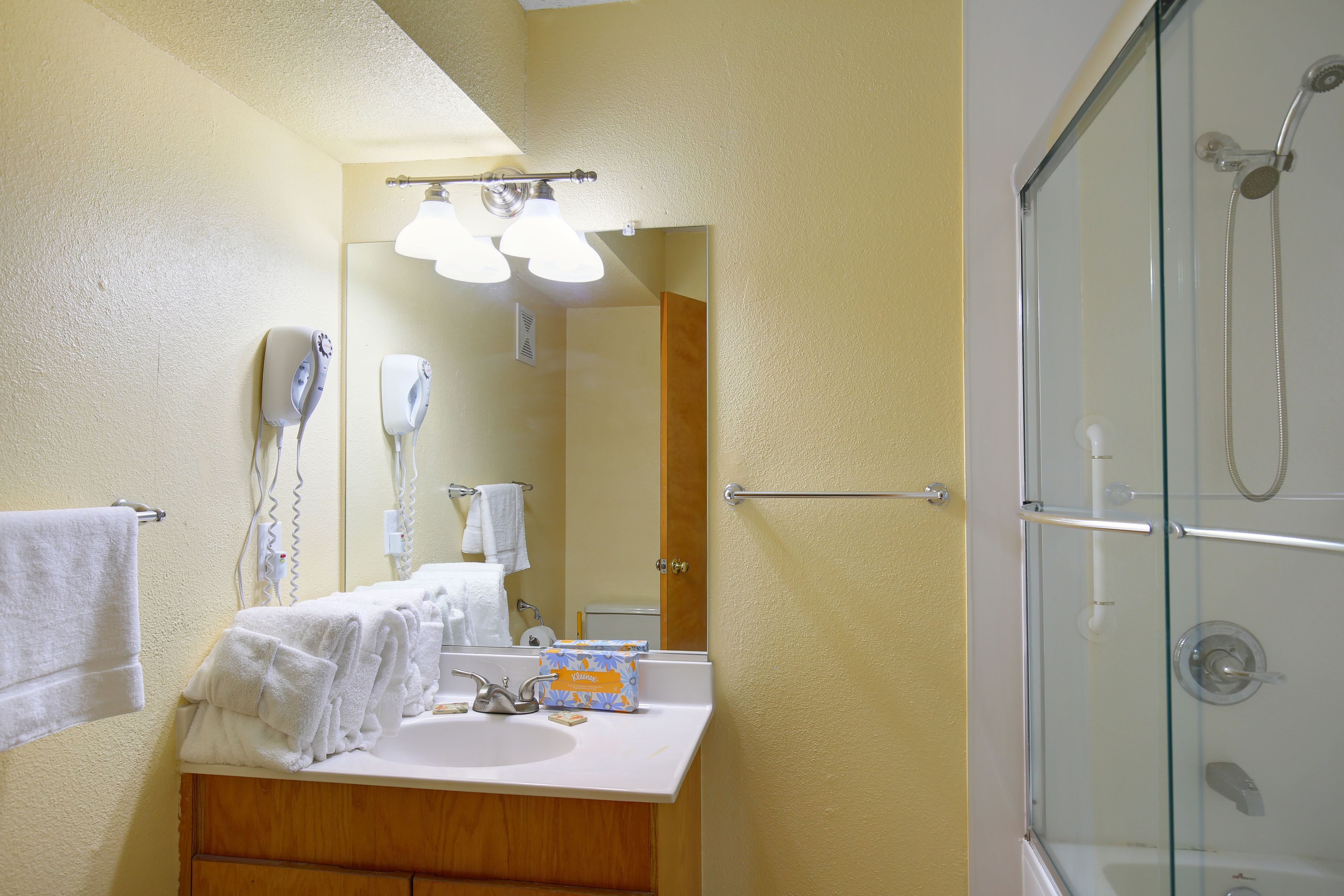 A bathroom with a sink, mirror, towel rack, and a glass-enclosed shower.