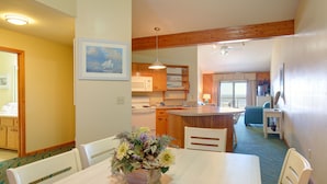 A dining area with a table and chairs, a kitchen in the background, and a view of the living area. - Ocean Pines Resort (Kitty Hawk)