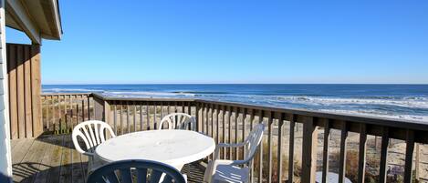 Une terrasse en bois avec une table et des chaises donnant sur la plage.