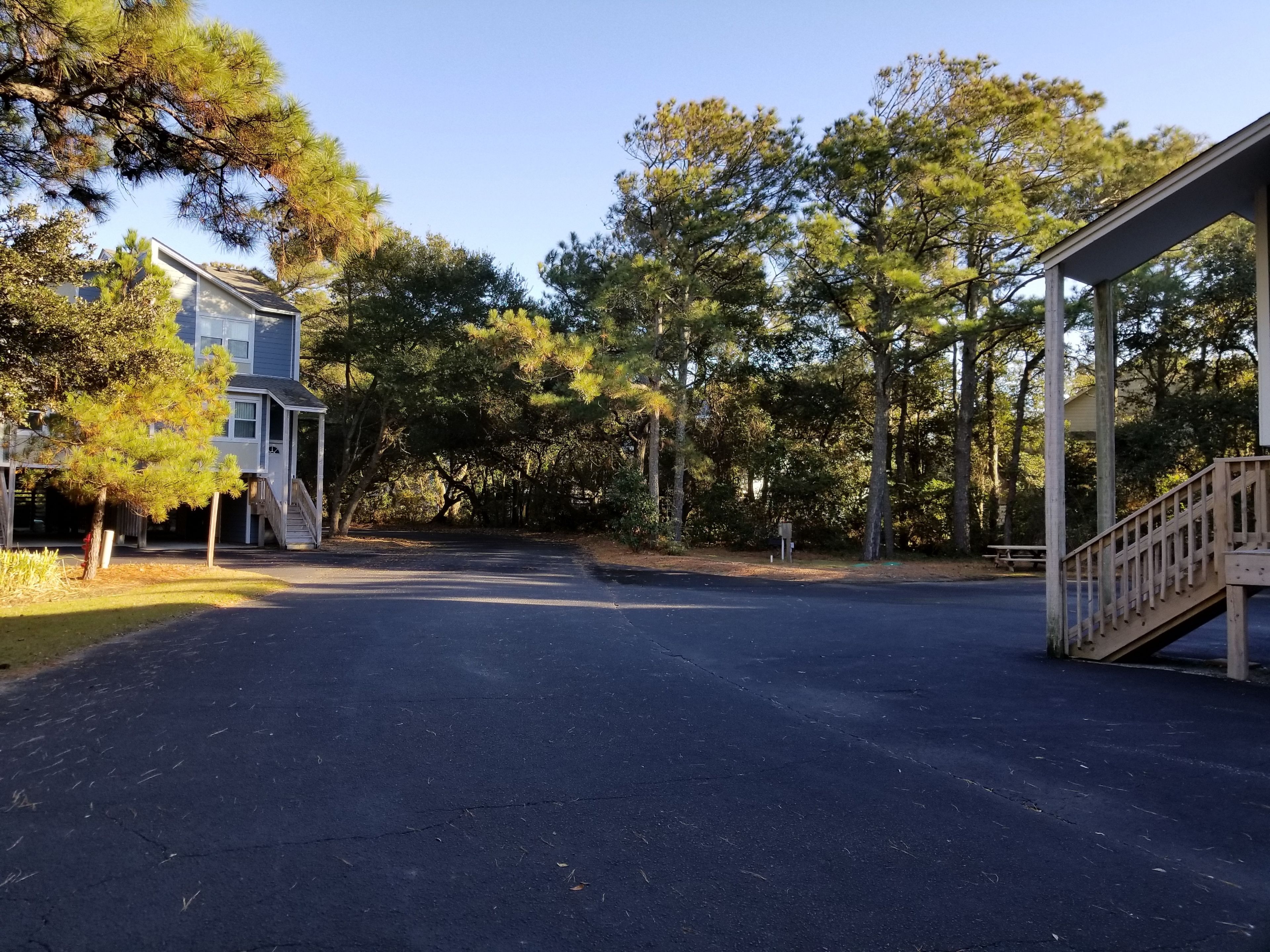 A residential street with a two-story house, a covered porch, and a staircase leading to a deck.