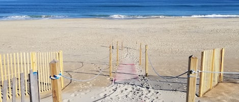 Een toegang tot het strand met houten poorten en een zandpad dat naar de oceaan leidt.