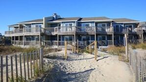 A beachfront property with multiple balconies, a sandy beach in front, and a wooden fence. - Ocean Pines Resort (Kitty Hawk)