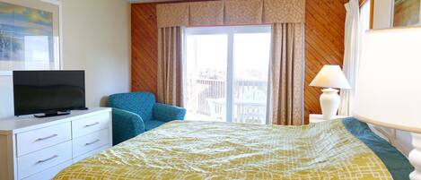 A hotel room with a bed, a TV on a dresser, a chair, a lamp, and a window with curtains.