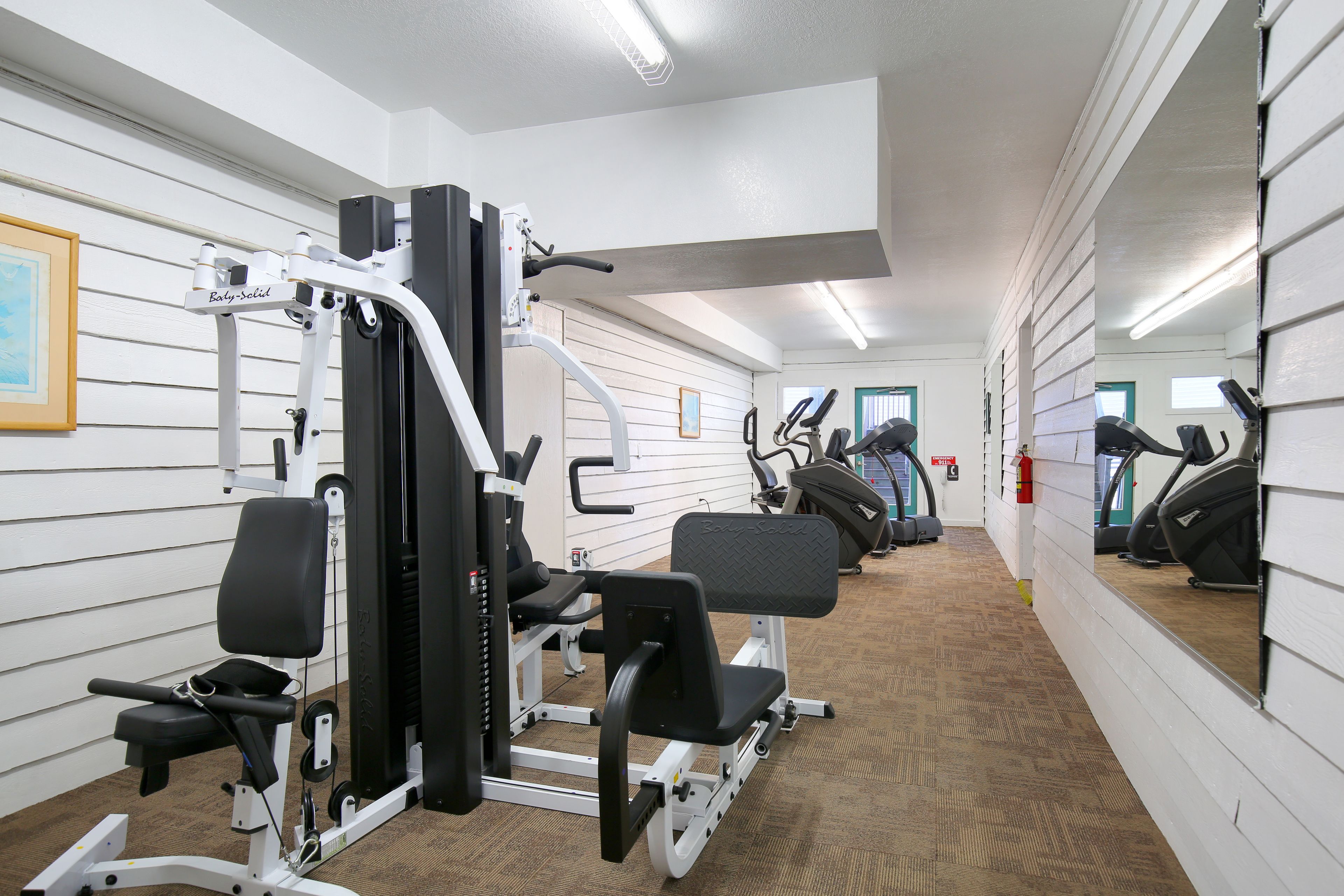 A gym with exercise equipment, including a bench press and a leg press, and a mirrored wall.
