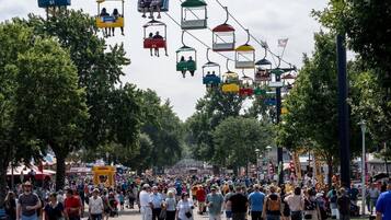 Un evento al aire libre concurrido, con gente caminando y teleféricos coloridos en lo alto.