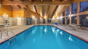 Une piscine intérieure avec des poutres en bois, des murs carrelés et un espace détente avec des tables et des chaises.