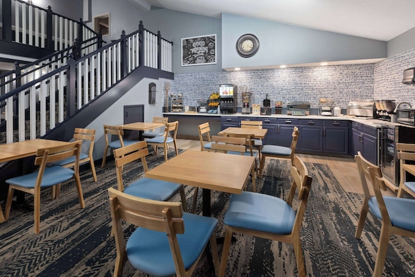 Una cocina moderna con protector mural de ladrillo, mesas y sillas de madera, y una escalera con barandillas negras.
