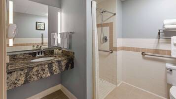 Baño con lavamanos de encimera de granito, espejo, ducha con barra de apoyo y un inodoro.