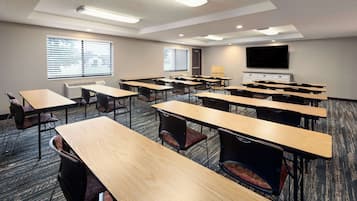 A conference room with multiple tables and chairs, a large flat-screen TV, and windows with blinds.