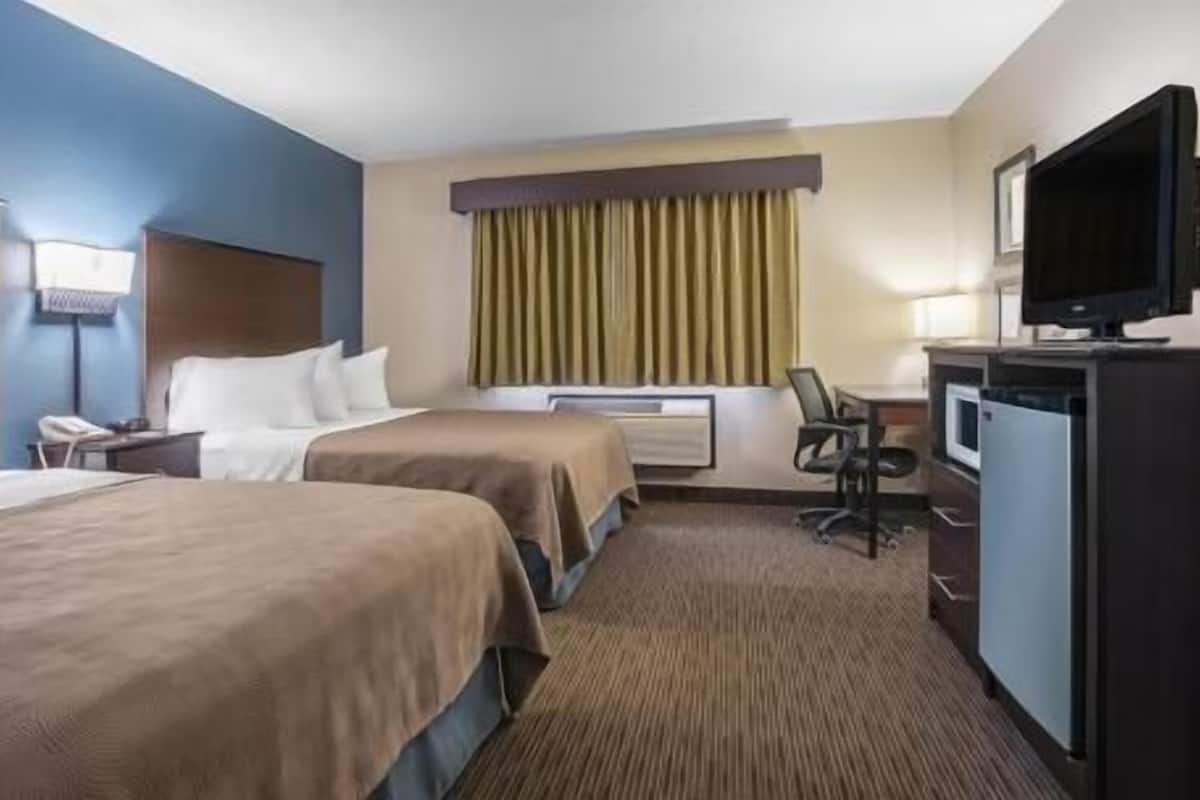 A hotel room with two beds, a desk, a chair, a television, and a window with curtains.