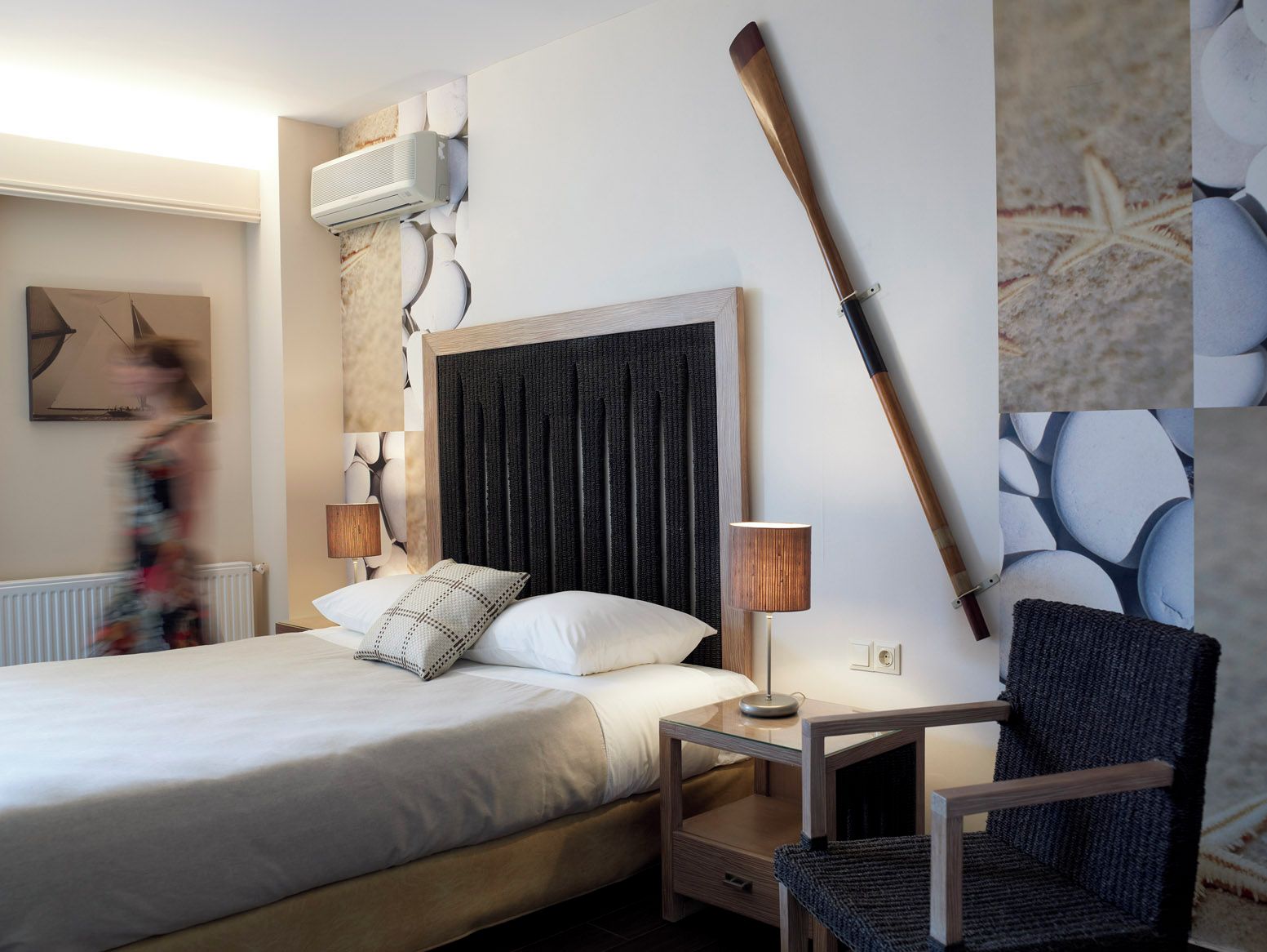 Ein Hotelzimmer mit einem Bett, einem Nachttisch, einer Lampe, einem Sessel und einer Wand-Klimaanlage.
