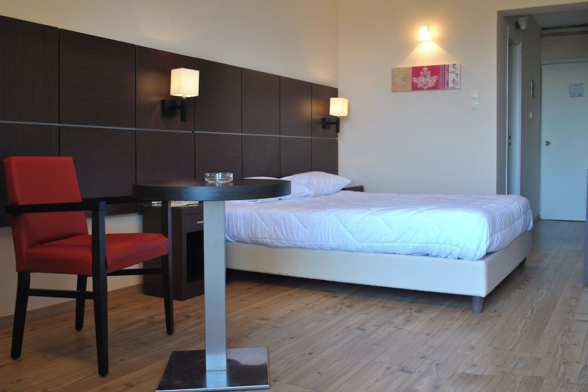 A hotel room with a bed, a desk with a chair, and two wall-mounted lamps.