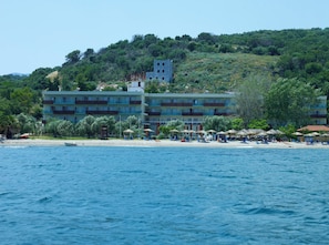 A hotel with multiple floors, a beach in the foreground, and a hillside in the background. - Belle Helene (East Mani)
