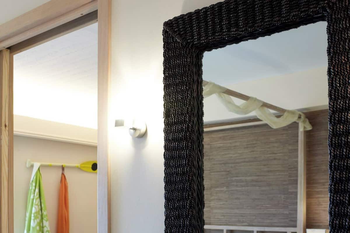 A hotel room with a large mirror, a bedside table with a vase of flowers, a bed, a nightstand, and a window with curtains.