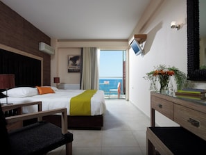 A hotel room with a bed, a desk, a chair, a TV, a plant, and a view of the sea. - Belle Helene (East Mani)