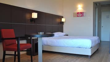 A hotel room with a bed, a desk with a chair, and two wall-mounted lamps.
